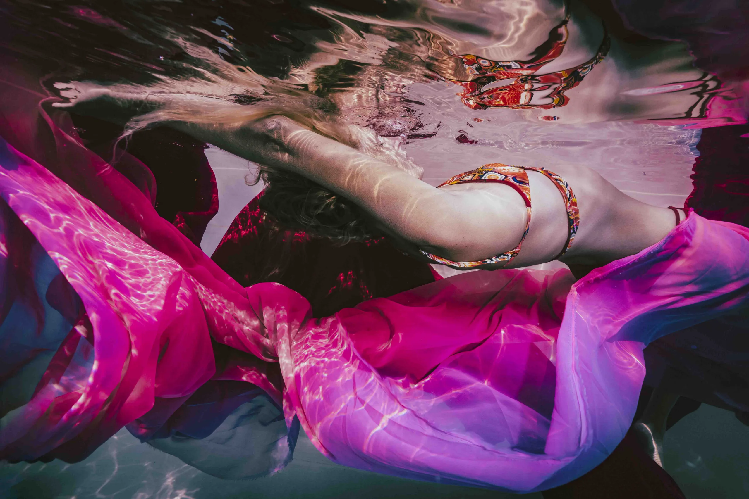 Underwater portrait of a woman draped in colorful fabrics, surrounded by vibrant hues