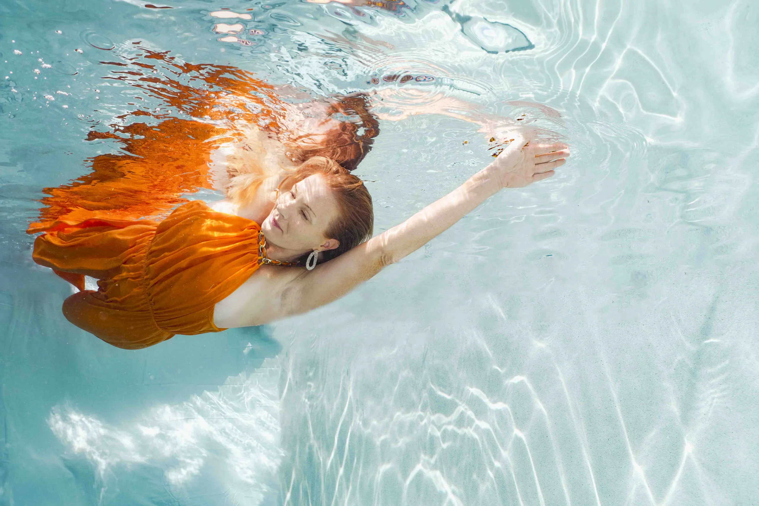 Colorful underwater fashion portrait featuring vibrant fabrics, with the model striking a powerful energetic pose.